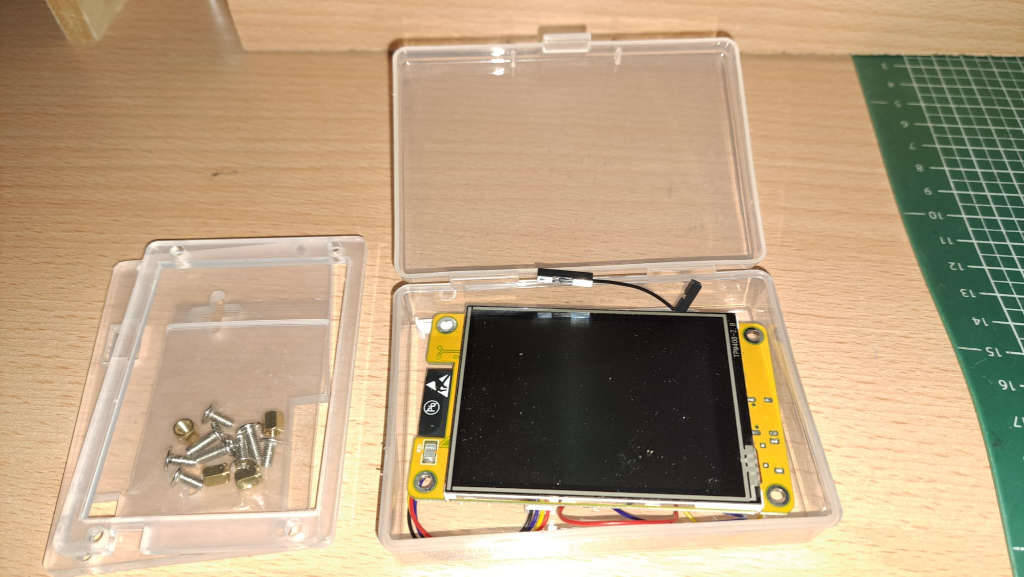 ESP32-2432S028R TFT-Board mit Touchscreen in der durchsichtigen Kunststoffbox, daneben Schrauben und Muttern in Beuteln